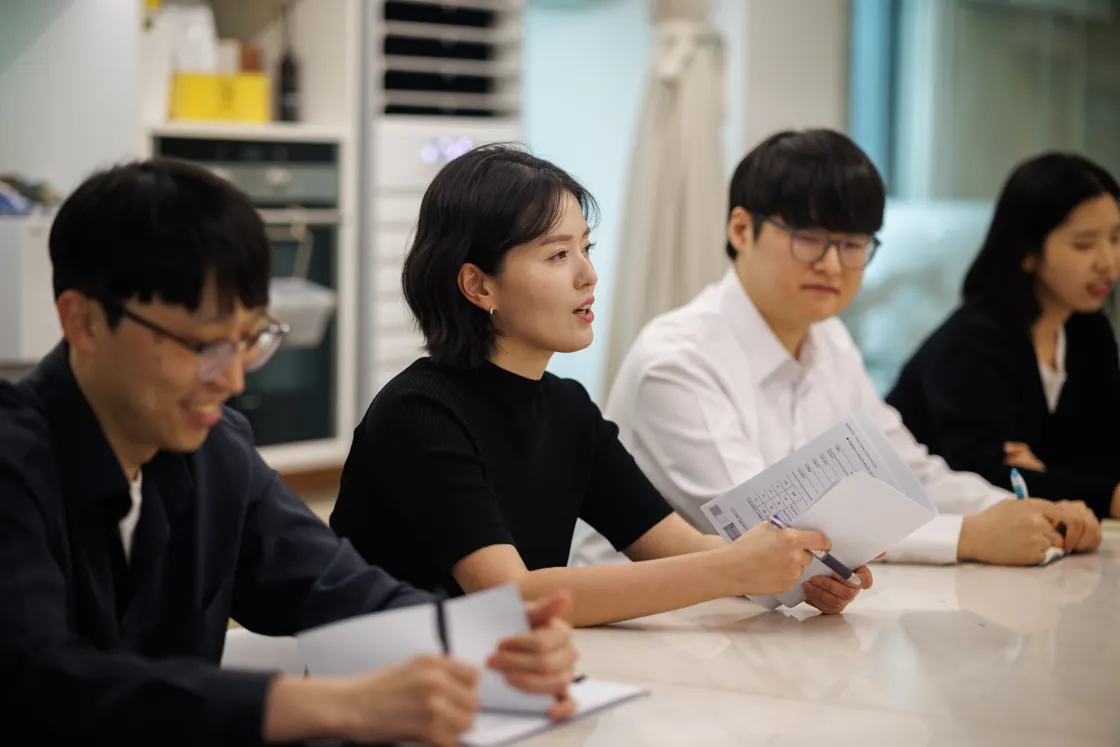 탁자에 나란히 앉아 웃으며 메모하는 회의 모습